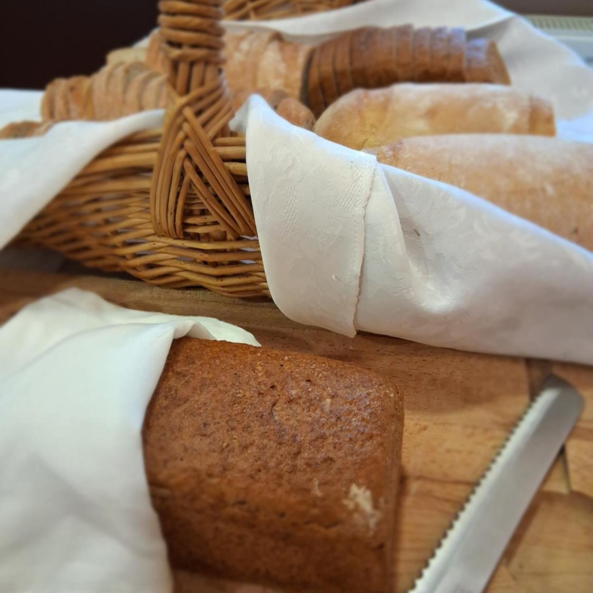 A basket of bread wrapped in white cloth, placed on a wooden surface.