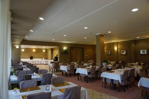 Ett rymligt matområde med flera bord och stolar, en scen för presentationer och en behaglig, varm belysning.