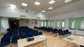 A conference room with rows of chairs, tables with projectors, and large windows with green curtains. - Geovita Centrum Konferencyjno - Rekreacyjne (Ladek-Zdrój)