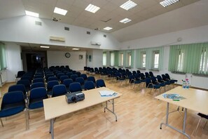 Ein Konferenzraum mit Reihen von Stühlen, Tischen mit Projektoren und großen Fenstern mit grünen Vorhängen.