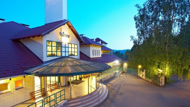 A hotel with a covered outdoor seating area, a staircase leading to the entrance, and a pathway flanked by trees. - Geovita Centrum Konferencyjno - Rekreacyjne (Ladek-Zdrój)