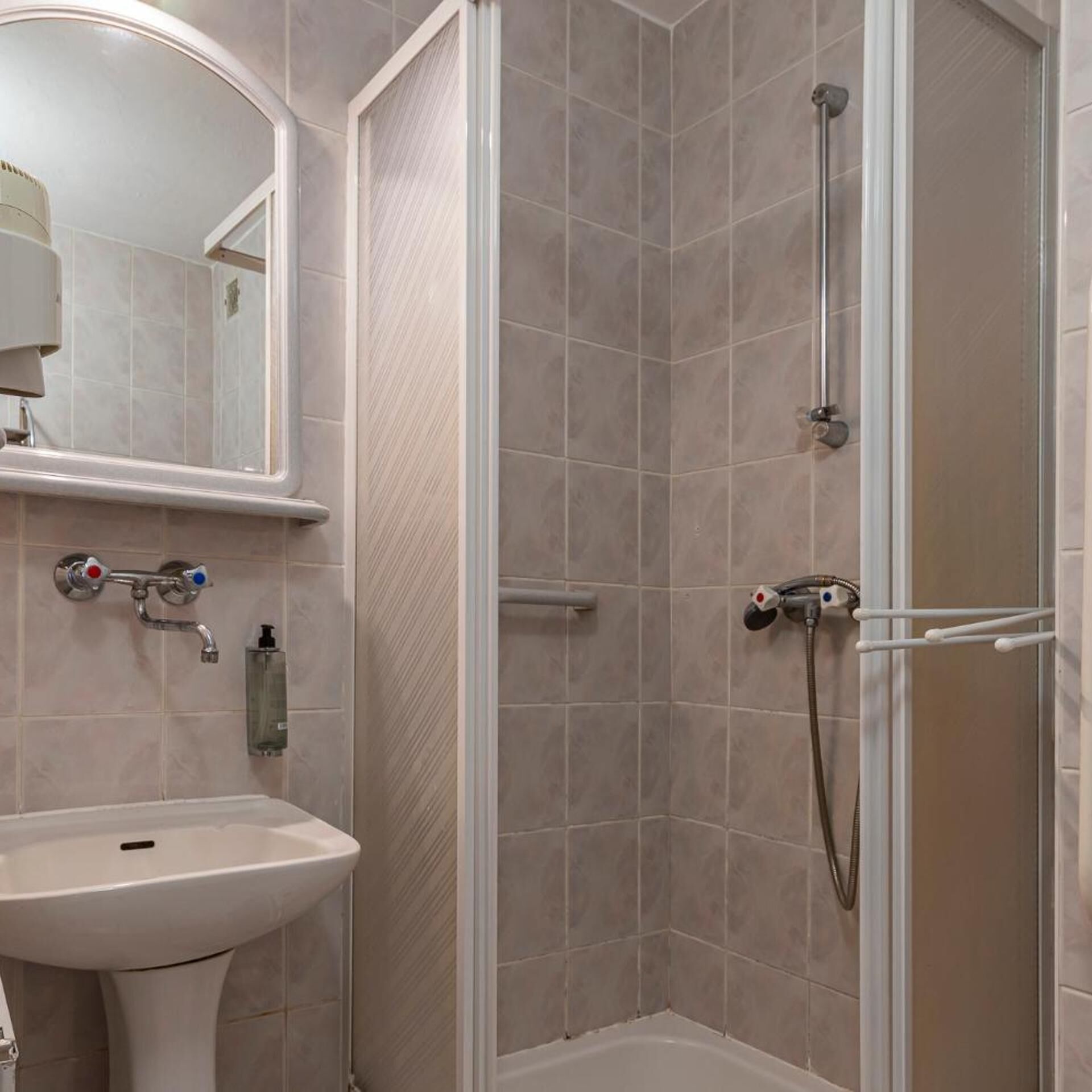 Un baño con lavamanos, espejo, ducha y paredes de azulejos.