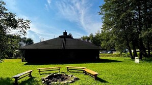 A building with a black roof, surrounded by a grassy area with picnic tables and a fire pit. - Geovita Centrum Konferencyjno - Rekreacyjne (Ladek-Zdrój)