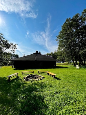 Ein Gebäude mit schwarzem Dach, umgeben von einer Grünfläche mit Picknicktischen und einem Feuerkorb.
