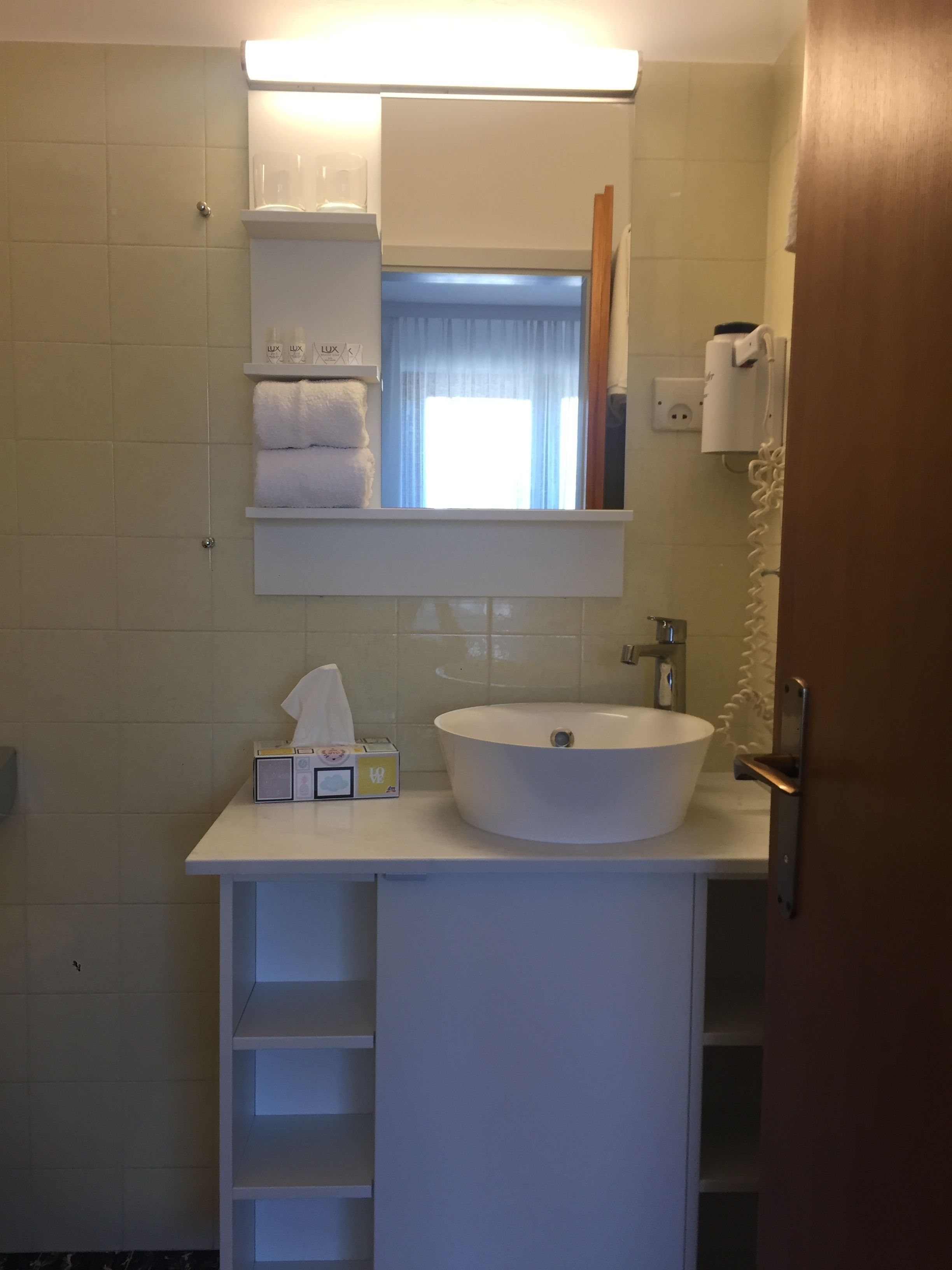 A bathroom with a white sink, a mirror above it, and a towel rack. There is a white cabinet below the mirror, and a door to the right.