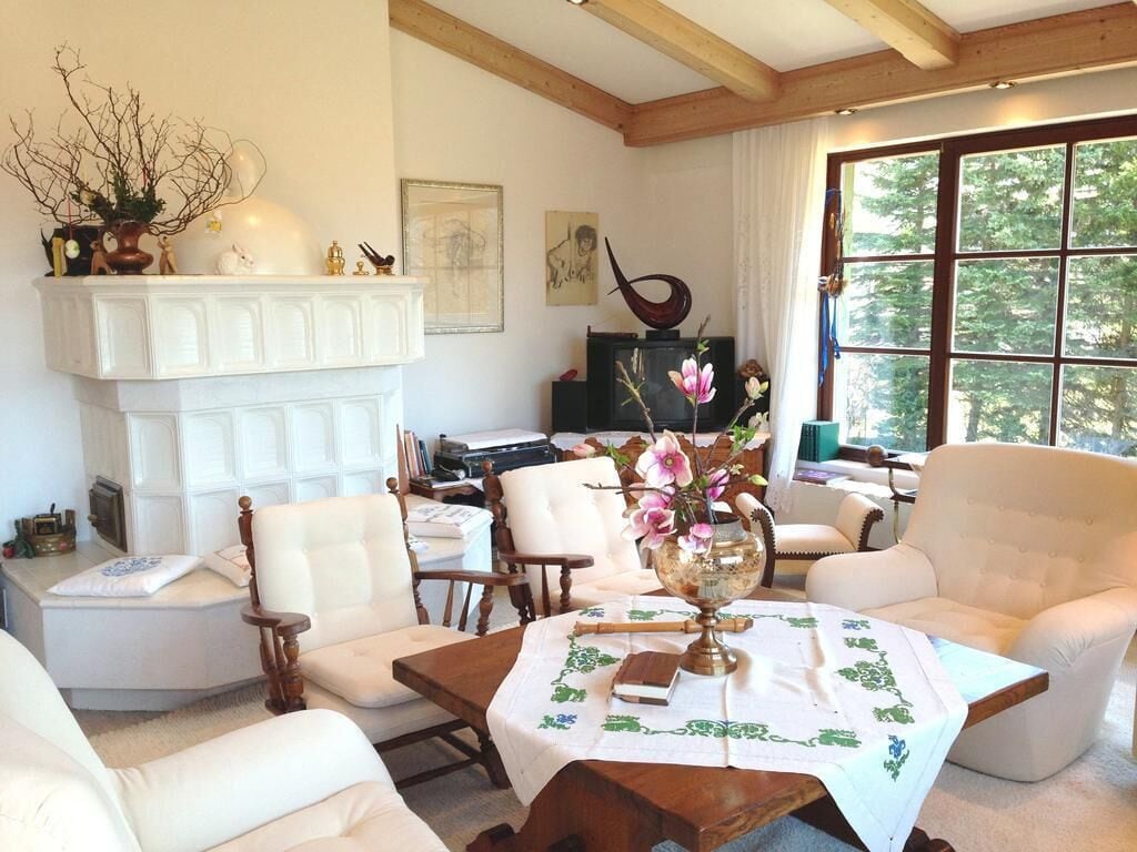 A cozy room with a fireplace, white furniture, and a large window with a view of trees.