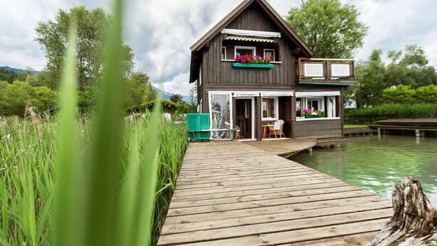 A wooden house with a balcony, a wooden deck, and a pond. - Dietrichsteinerhof Apartments & Rooms (Finkenstein am Faaker See)