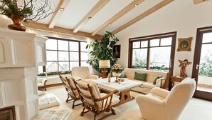 A spacious living room with a fireplace, wooden furniture, and large windows offering a view of the outdoors. - Dietrichsteinerhof Apartments & Rooms (Finkenstein am Faaker See)