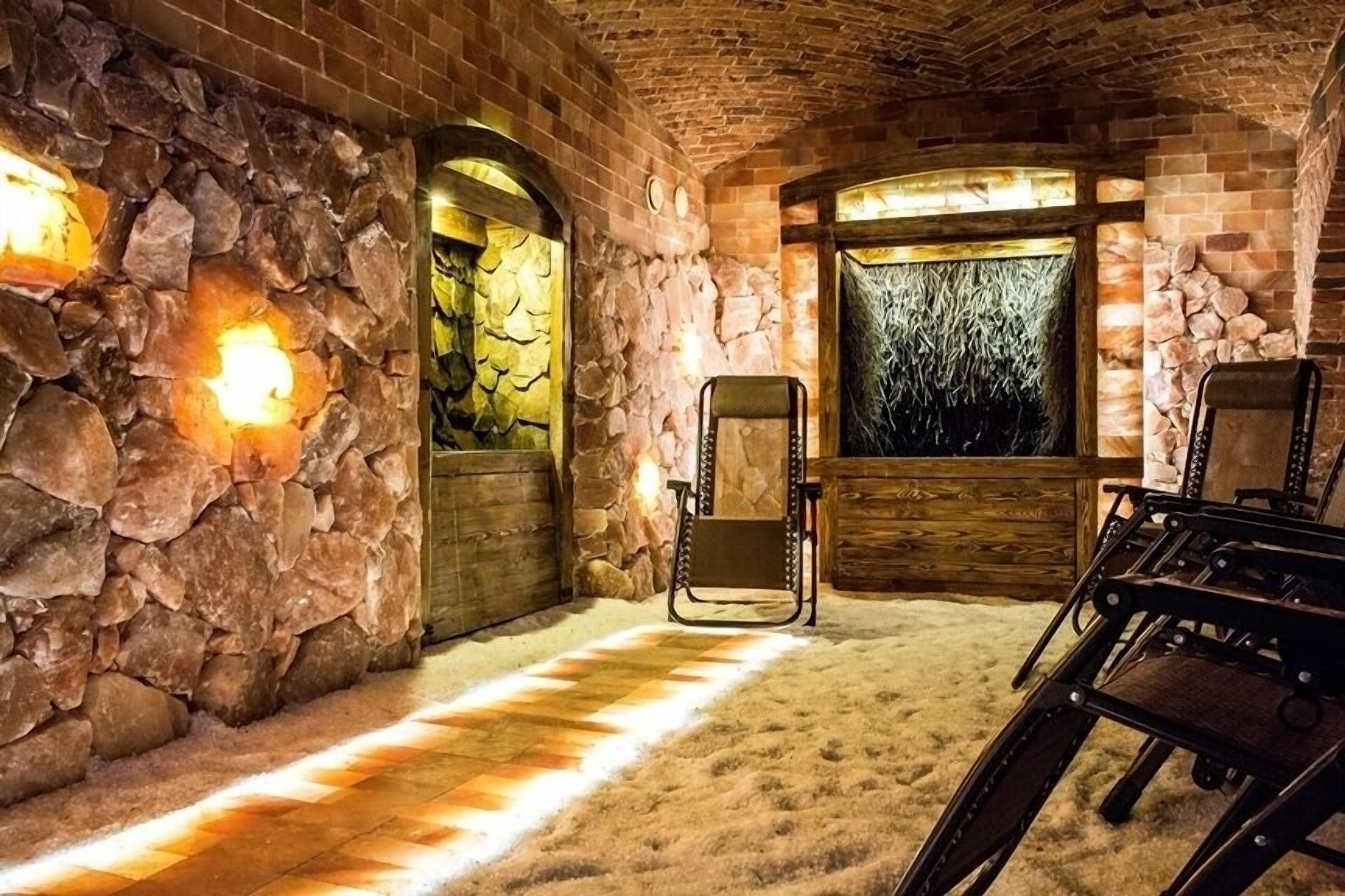 A stone-walled room with a fireplace, a wooden chair, and a view through a window.
