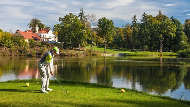 Um campo de golfe com lago, árvores e um edifício ao fundo.