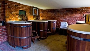 Quarto com paredes de tijolo, barris de madeira e uma banheira branca.