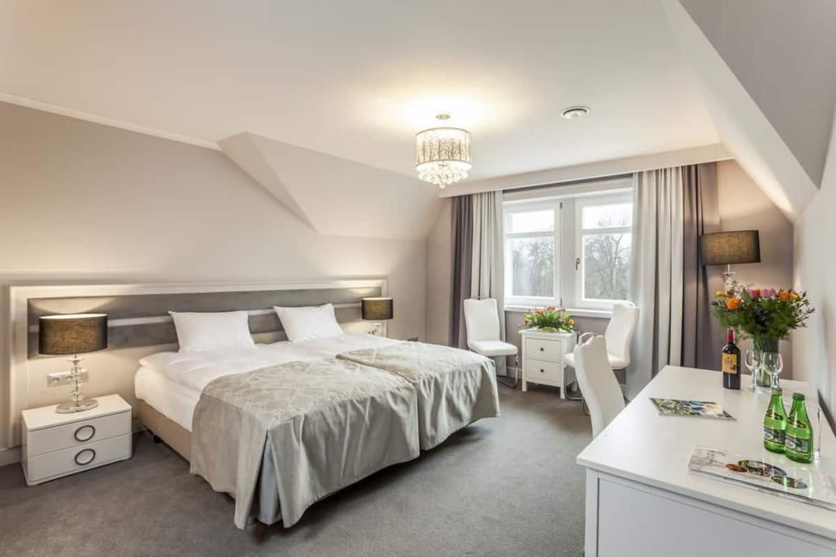 Moderni hotellihuone, jossa on suuri sänky, yöpöydät, työpöytä, tuoli ja ikkuna, jossa on verhot.