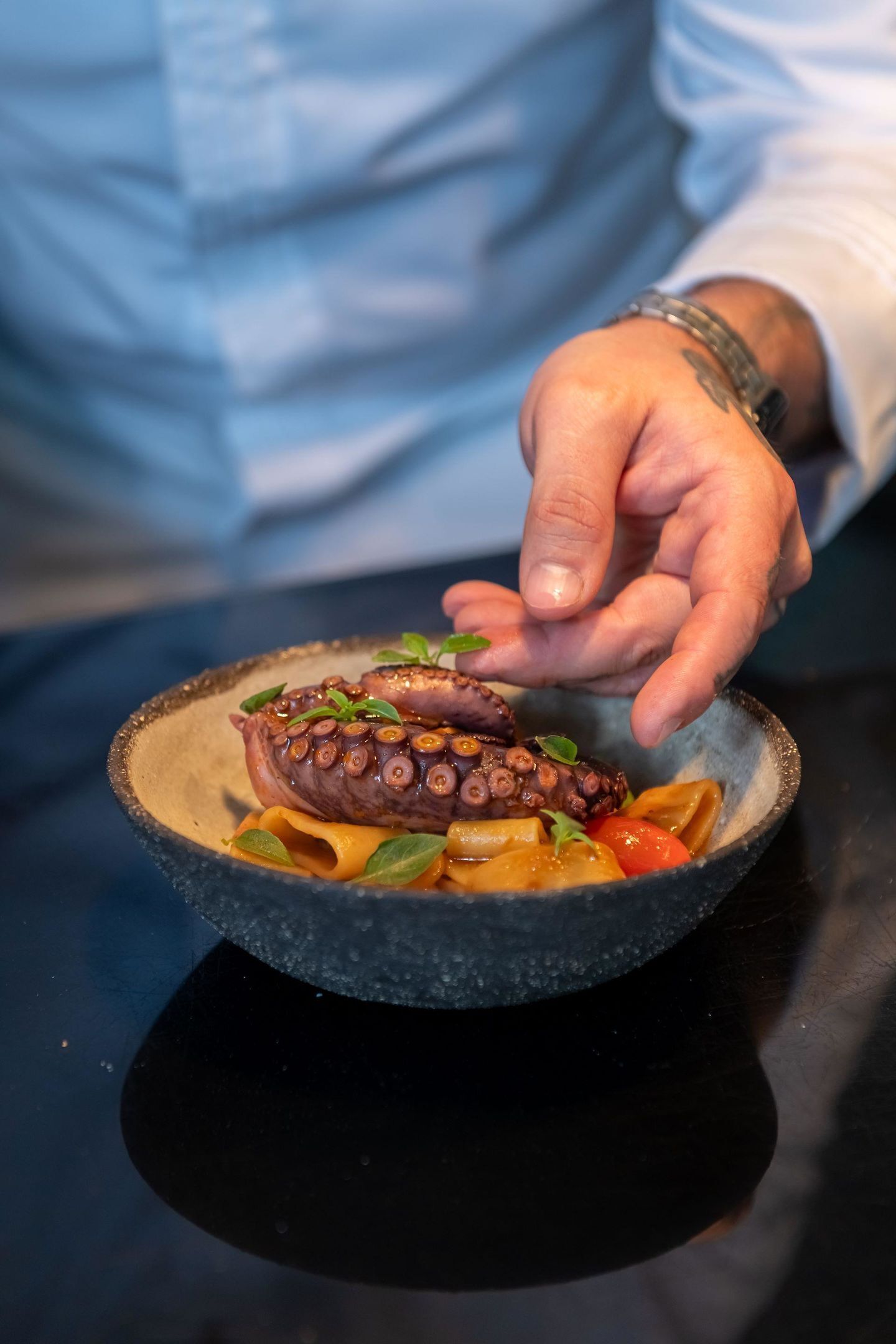 Una mano sostiene un bol con pulpo y pasta.
