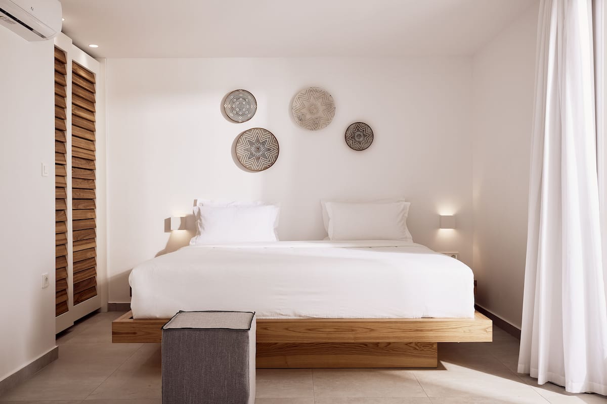 Ein modernes Schlafzimmer mit einem hölzernen Plattformbett, weißer Bettwäsche und drei an der Wand befestigten Dekotellern.
