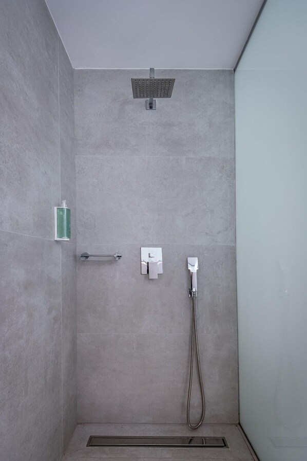 A shower area with a handheld showerhead, a soap dispenser, and a towel rack.