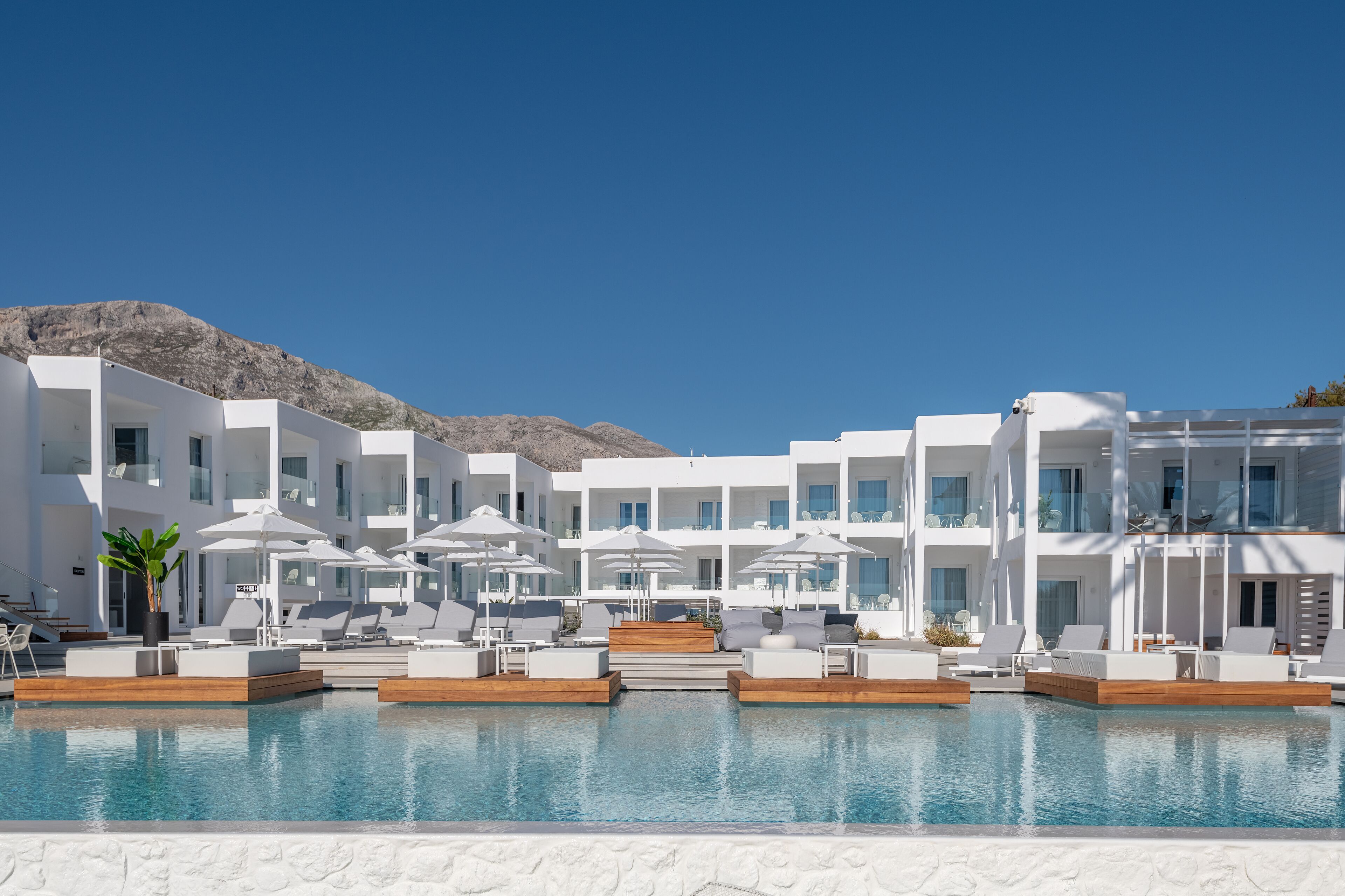A modern hotel with a pool area, white buildings, and a mountain in the background.