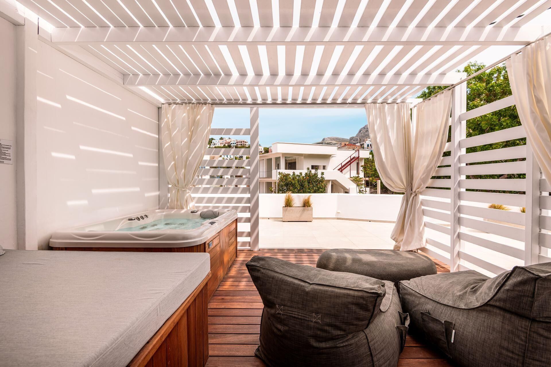 A modern outdoor relaxation area with a hot tub, wooden flooring, and cushioned seating.