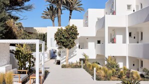 Un edificio moderno blanco con balcones, una zona de estar cubierta y diversas plantas.