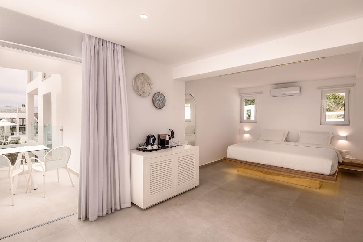 Ein modernes Schlafzimmer mit einem großen Bett, einer weißen Kommode und einem Essbereich mit Stühlen.