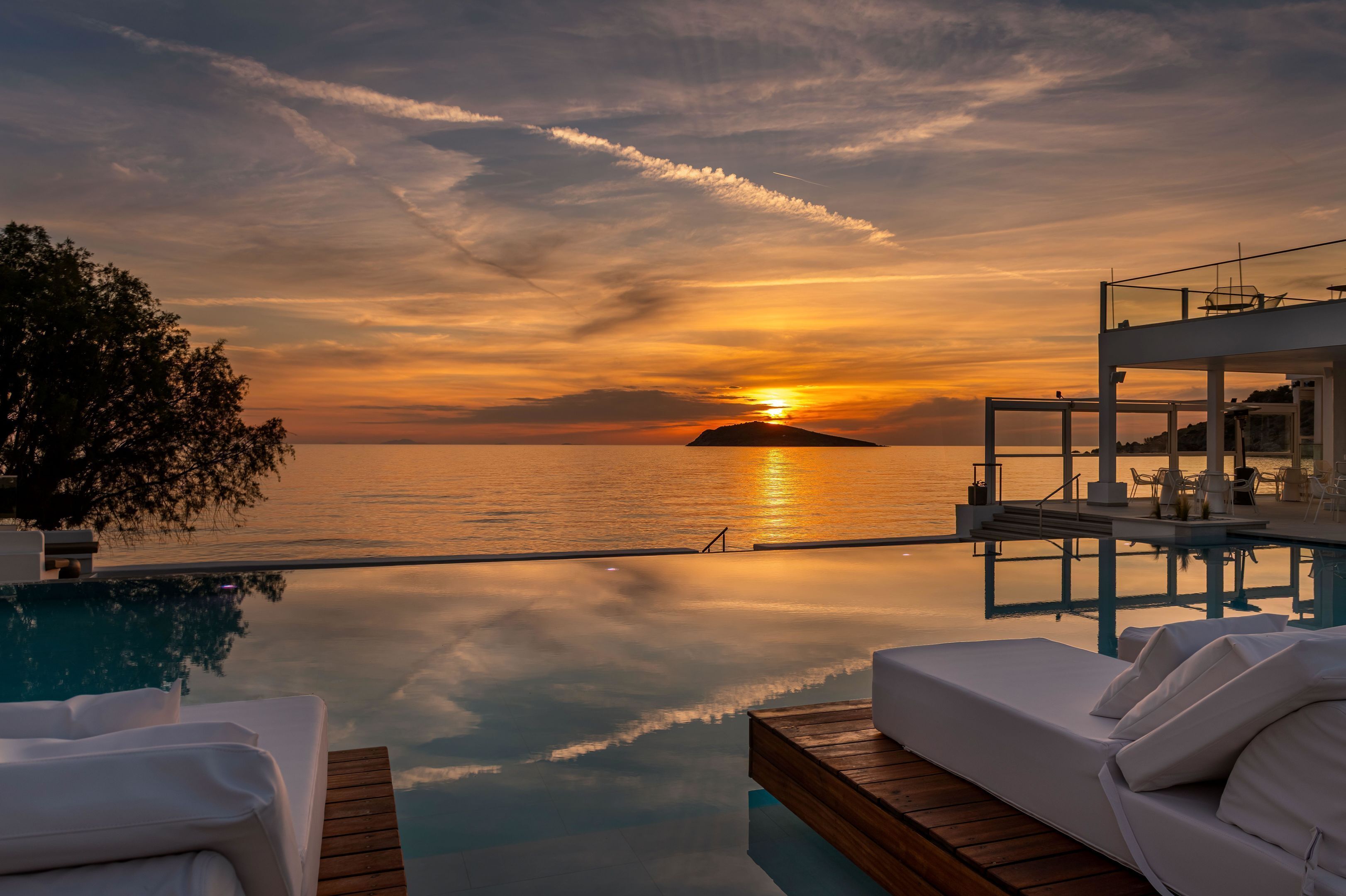Una piscina infinita con vistas al atardecer, sillones de descanso y una terraza de madera.