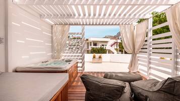 Un patio moderno al aire libre con una terraza de madera, un jacuzzi y zonas de estar con cojines.