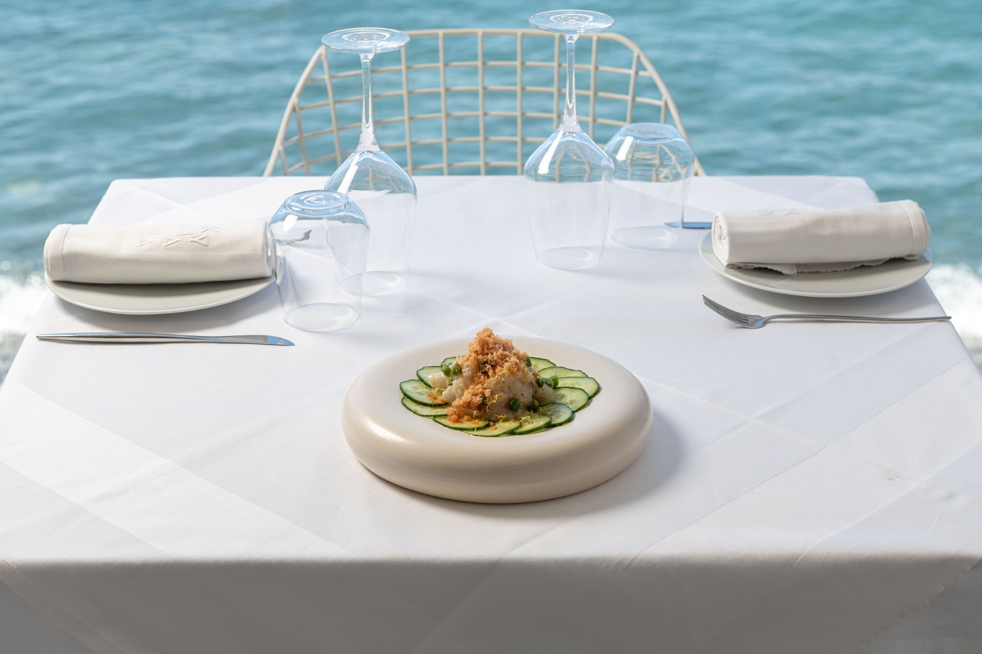 Una mesa vestida con un mantel blanco, un plato de comida y copas de vino vacías.
