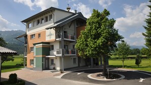 A multi-story building with a balcony, surrounded by greenery and mountains in the background. - Karglhof - Stammhaus (Finkenstein am Faaker See)