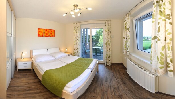 A bedroom with a bed, bedside tables, a window with curtains, a balcony, and a ceiling light fixture. - Karglhof - Stammhaus (Finkenstein am Faaker See)