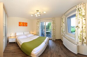 Un dormitorio con cama, mesitas de noche, una ventana con cortinas, un balcón y una lámpara en el techo.