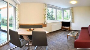 A room with a dining table, two chairs, a red sofa, a TV, and large windows with curtains. - Karglhof - Stammhaus (Finkenstein am Faaker See)