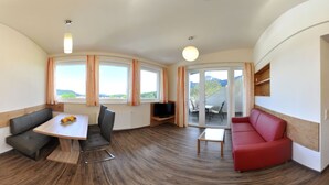 A modern living room with a wooden door, a dining table with chairs, a red sofa, and large windows with curtains. - Karglhof - Stammhaus (Finkenstein am Faaker See)