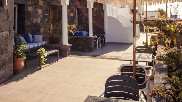 Un patio moderno al aire libre con paredes de piedra, columnas blancas y un área de estar con sombrillas.