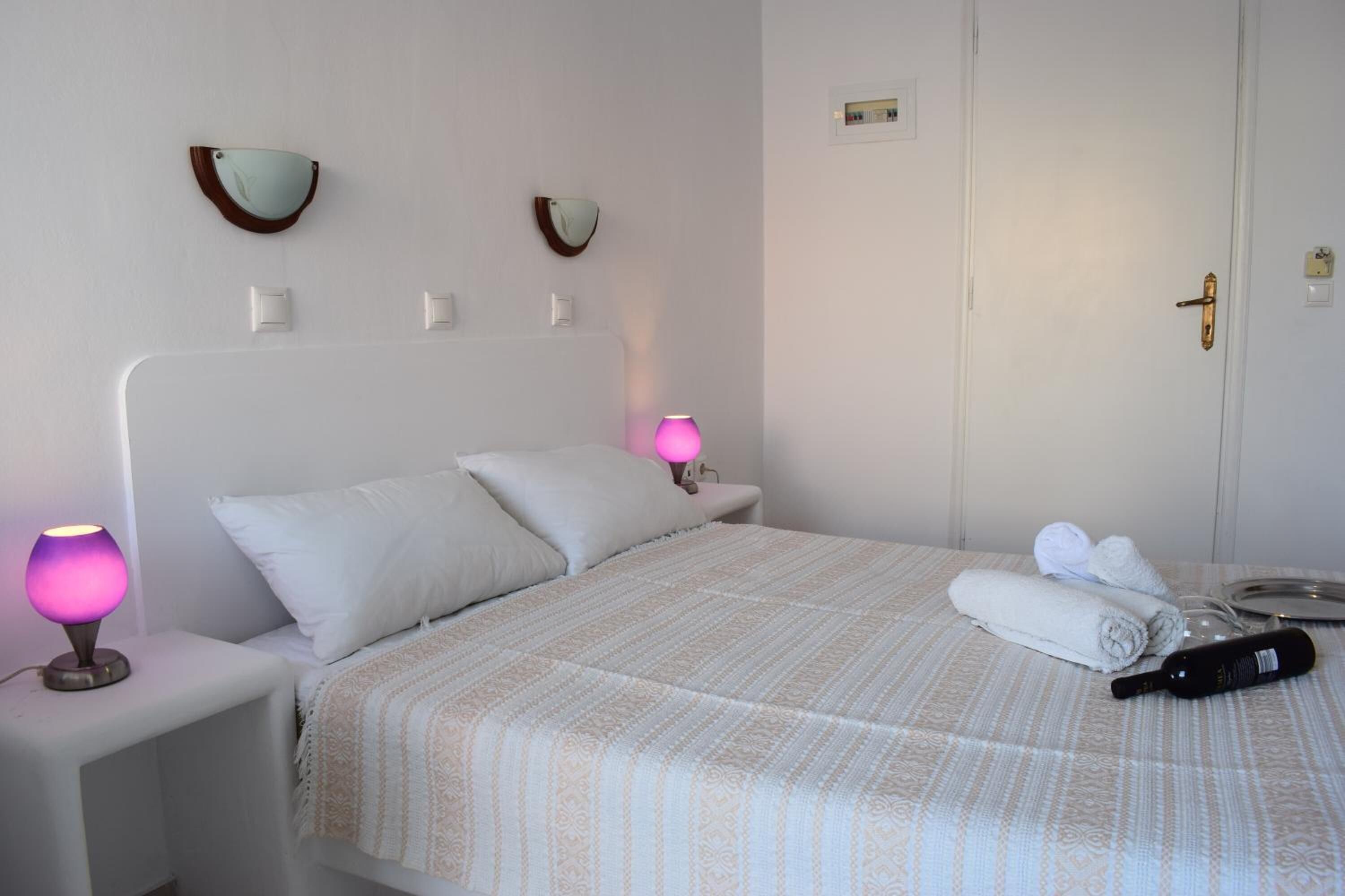 A neatly made bed with a patterned bedspread, two bedside lamps, and a bottle on the bed.