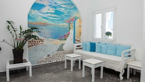 Una habitación con un mural de paisaje costero, un sofá blanco con cojines azules y una mesita.