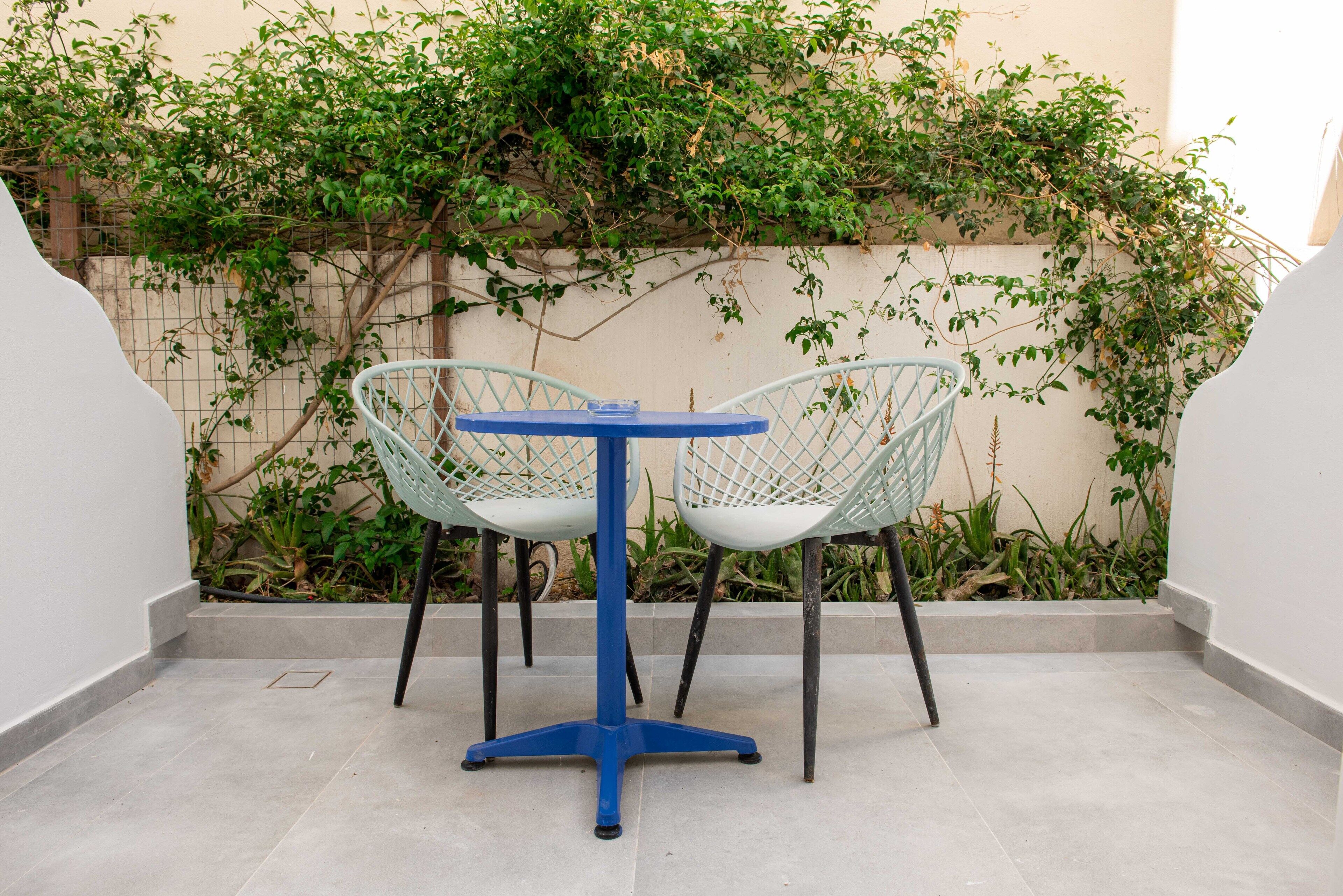 A small outdoor seating area with a round table and two chairs, surrounded by a low wall and greenery.