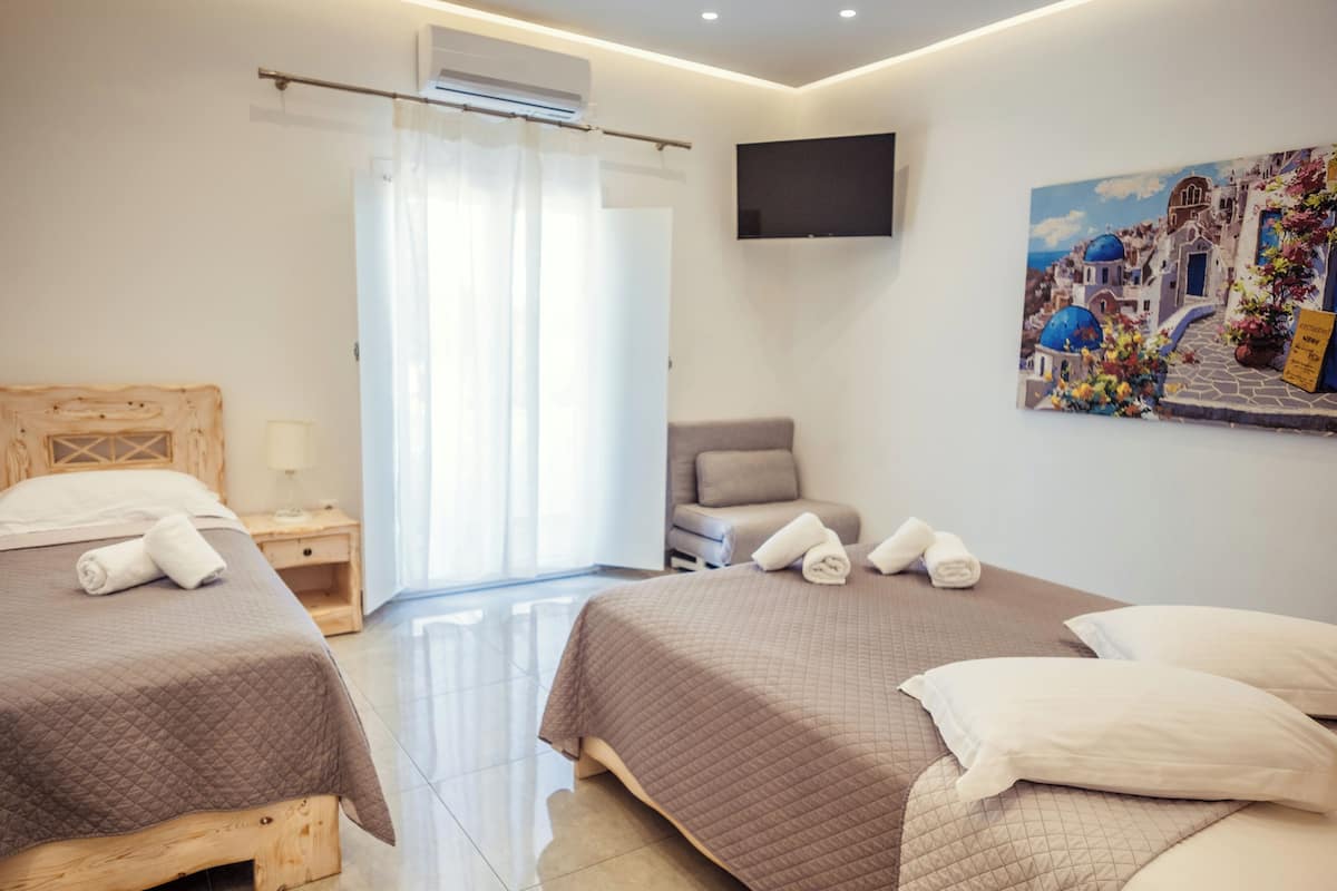 A hotel room with two beds, a TV mounted on the wall, and a painting of a coastal scene.