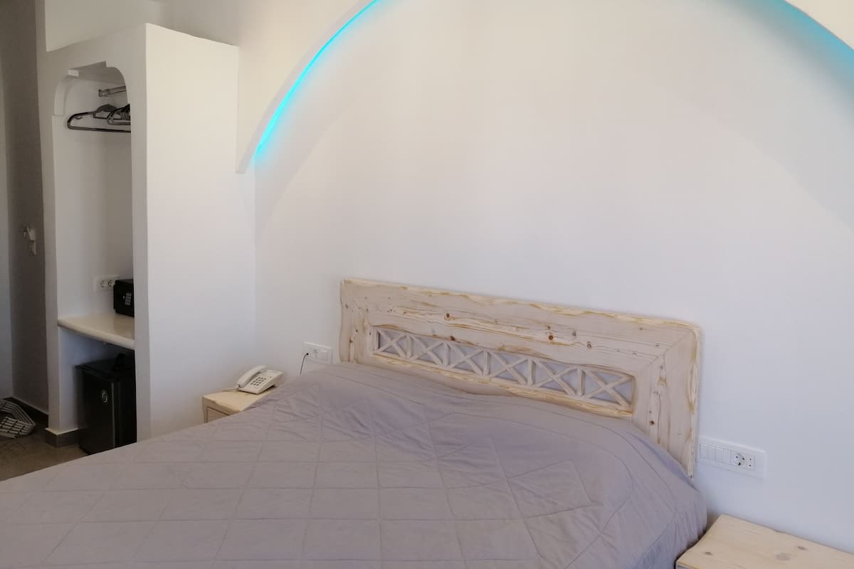 A bedroom with a bed, a nightstand, a wooden headboard, and a curved light fixture.