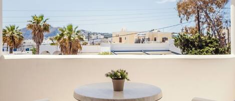 A balcony with a round table and two white chairs, overlooking a cityscape with buildings and palm trees.