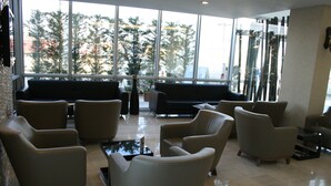 A spacious lobby with multiple seating areas, large windows offering a view of trees and buildings, and a clean, modern design. - Gosterisli Hotel (Düzce)