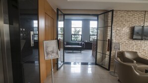A modern hotel lobby with a glass partition, a sofa, a television, and a menu stand. - Gosterisli Hotel (Düzce)