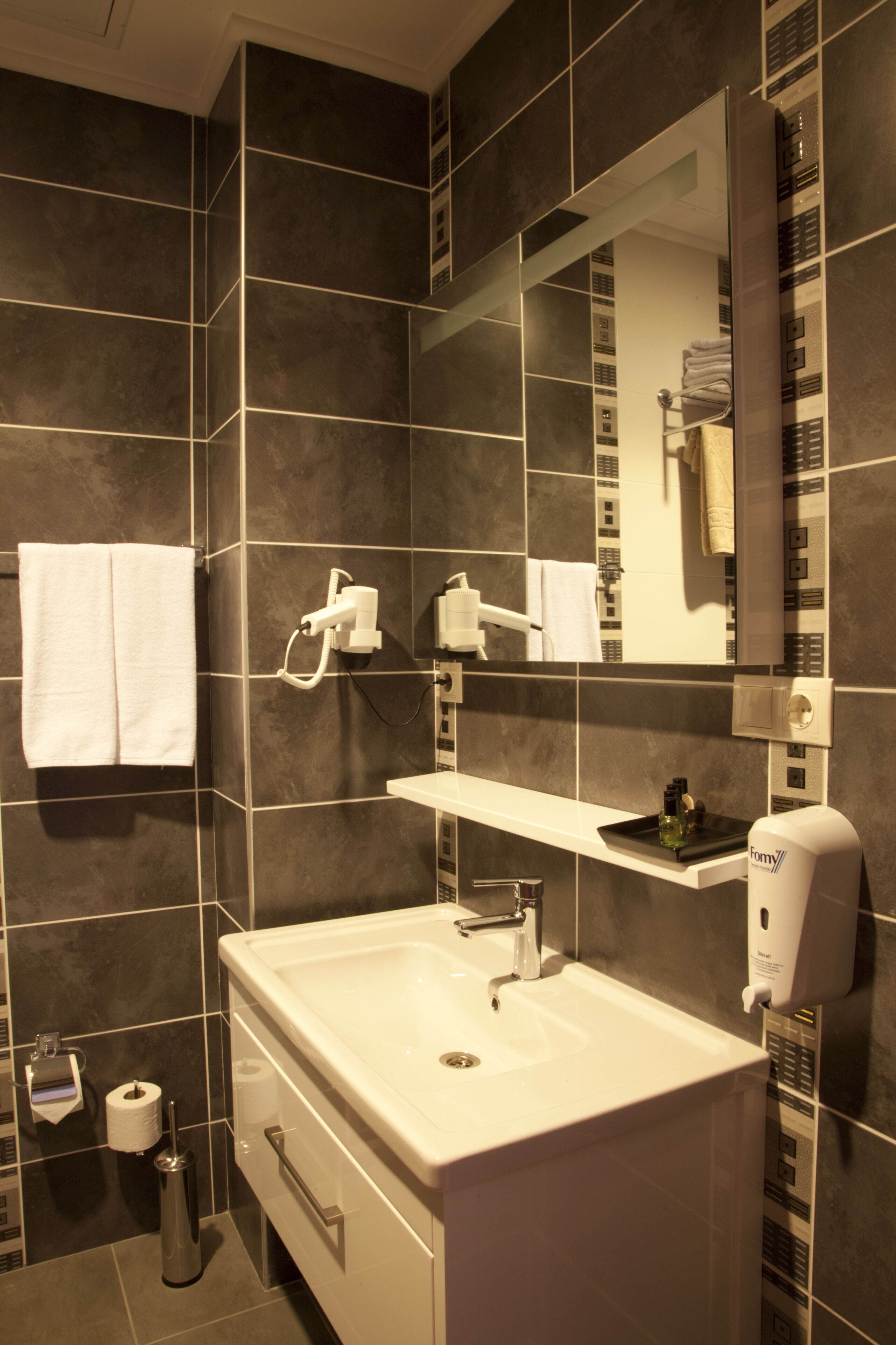 Een moderne badkamer met een grote spiegel, een witte wastafel en een handdoekhouder.