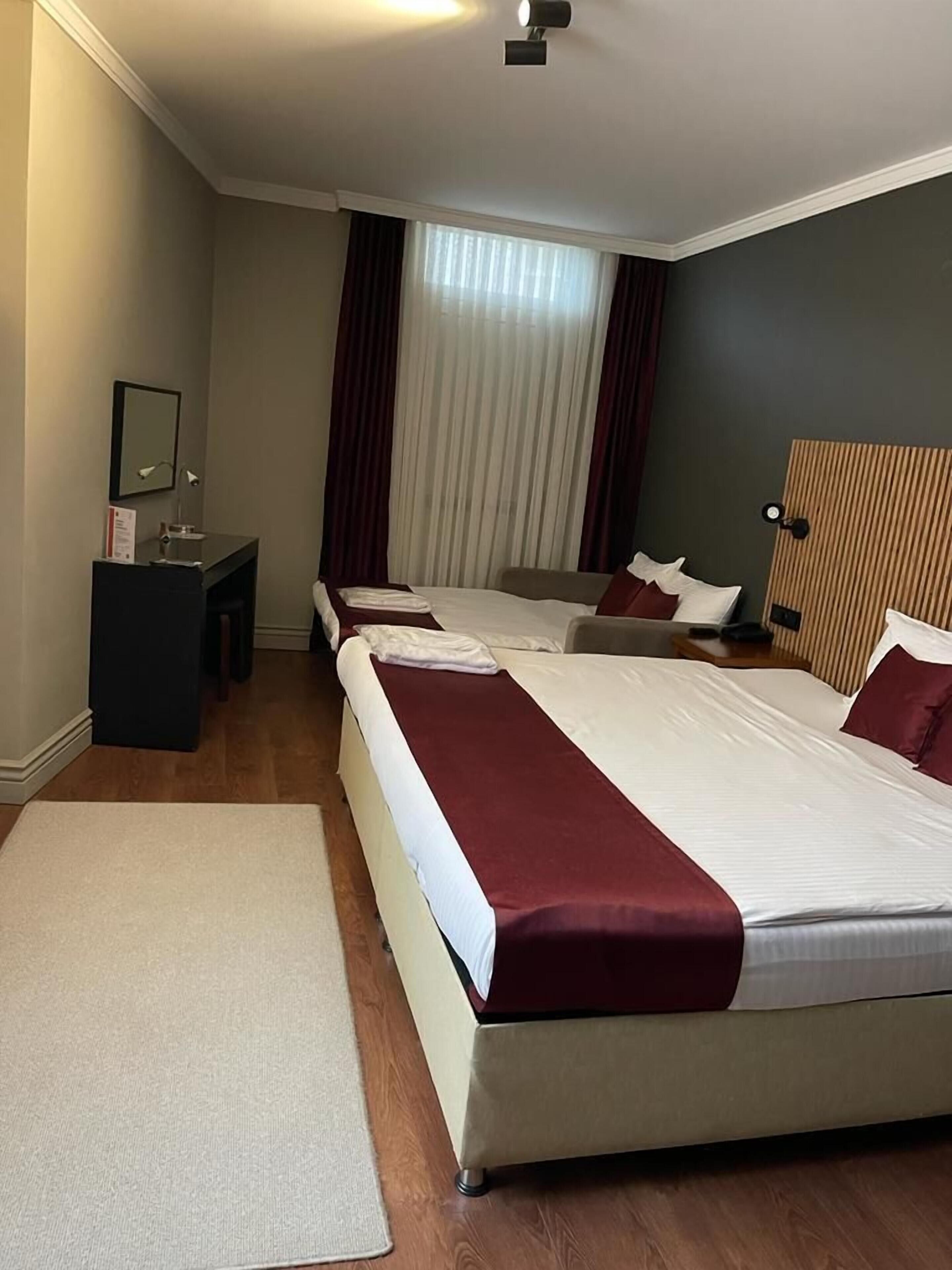 Een hotelkamer met twee bedden, een bureau, een spiegel en een raam met gordijnen.