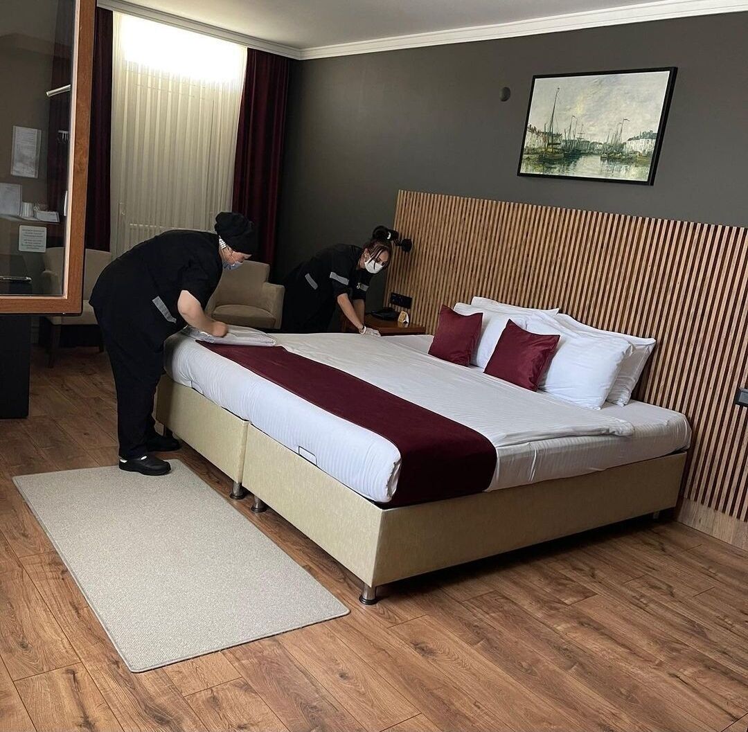 Una habitación de hotel con cama, escritorio, silla, ventana con cortinas y un cuadro en la pared.