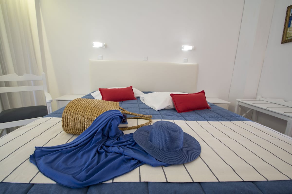 A neatly made bed with a striped bedspread, two red pillows, and a woven basket.