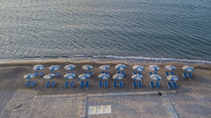 Vue aérienne d’une plage avec des rangées de chaises longues bleues et des parasols blancs et bleus.