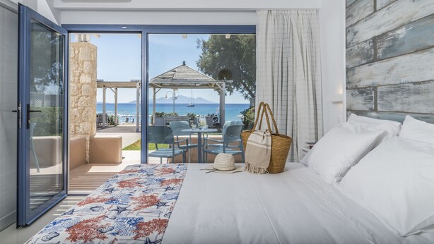 A bedroom with a bed, a large window, and a view of the sea. - Kordistos Hotel (Kos)