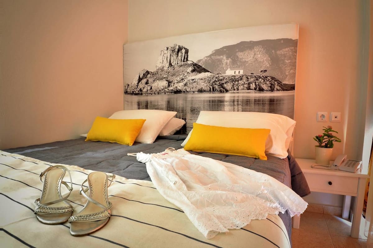 A bedroom with a bed, pillows, a nightstand, a phone, and a painting of a landscape.