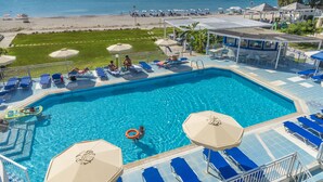 A swimming pool with blue lounge chairs and umbrellas, a beach in the background, and a view of the sea. - Kordistos Hotel (Kos)