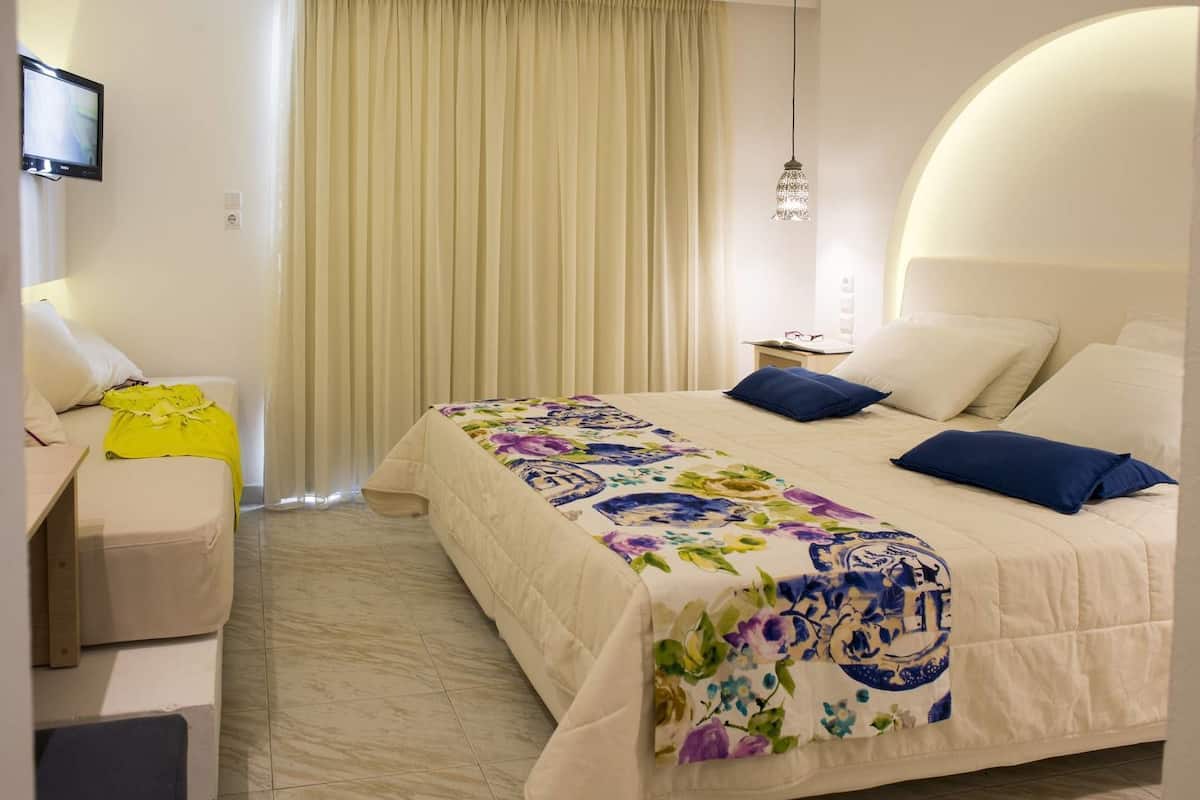 A hotel room with a bed, a desk, a chair, a TV, and a window with curtains.