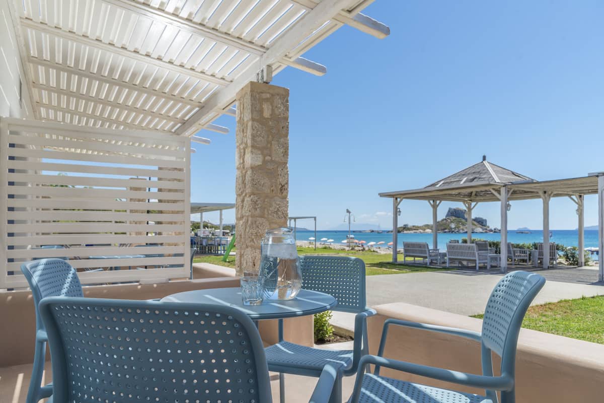 An outdoor seating area with blue chairs and a table, overlooking a beach and the sea.